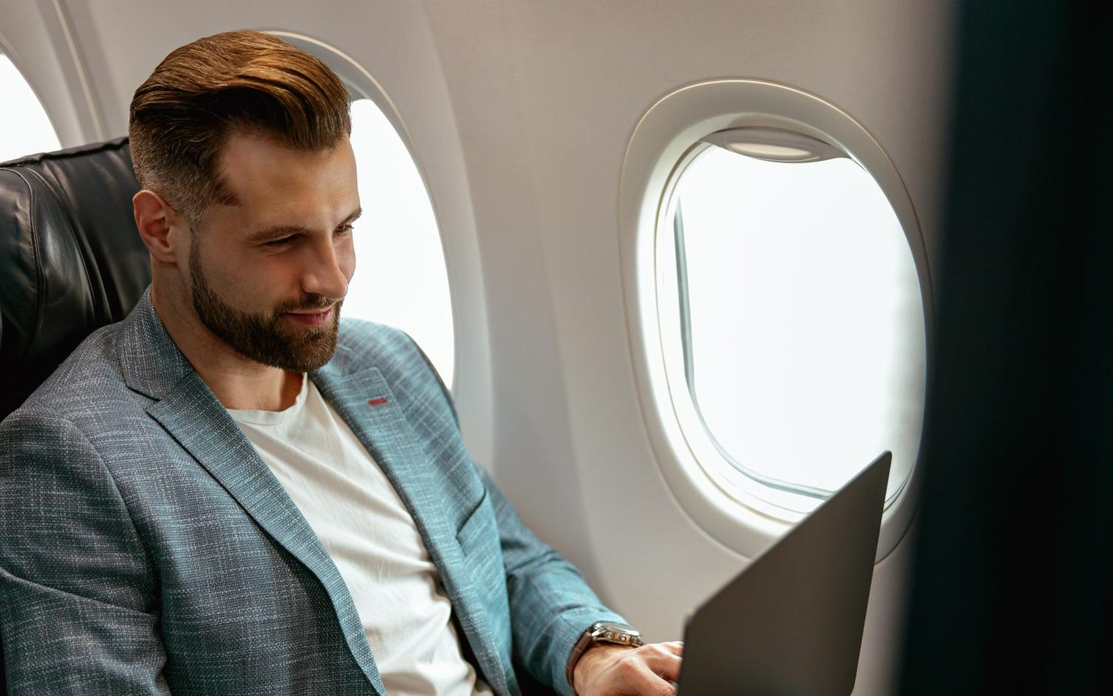 A traveller working on a laptop by an aircraft window