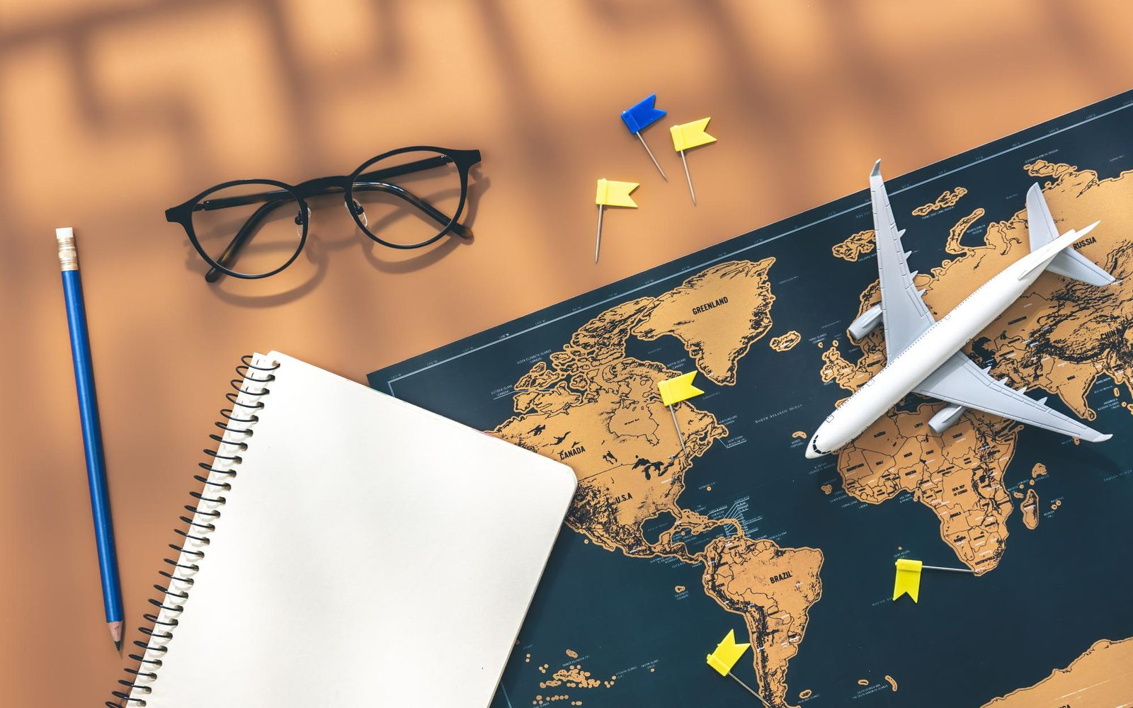 A desk with a world map, a model aircraft, glasses and a notebook