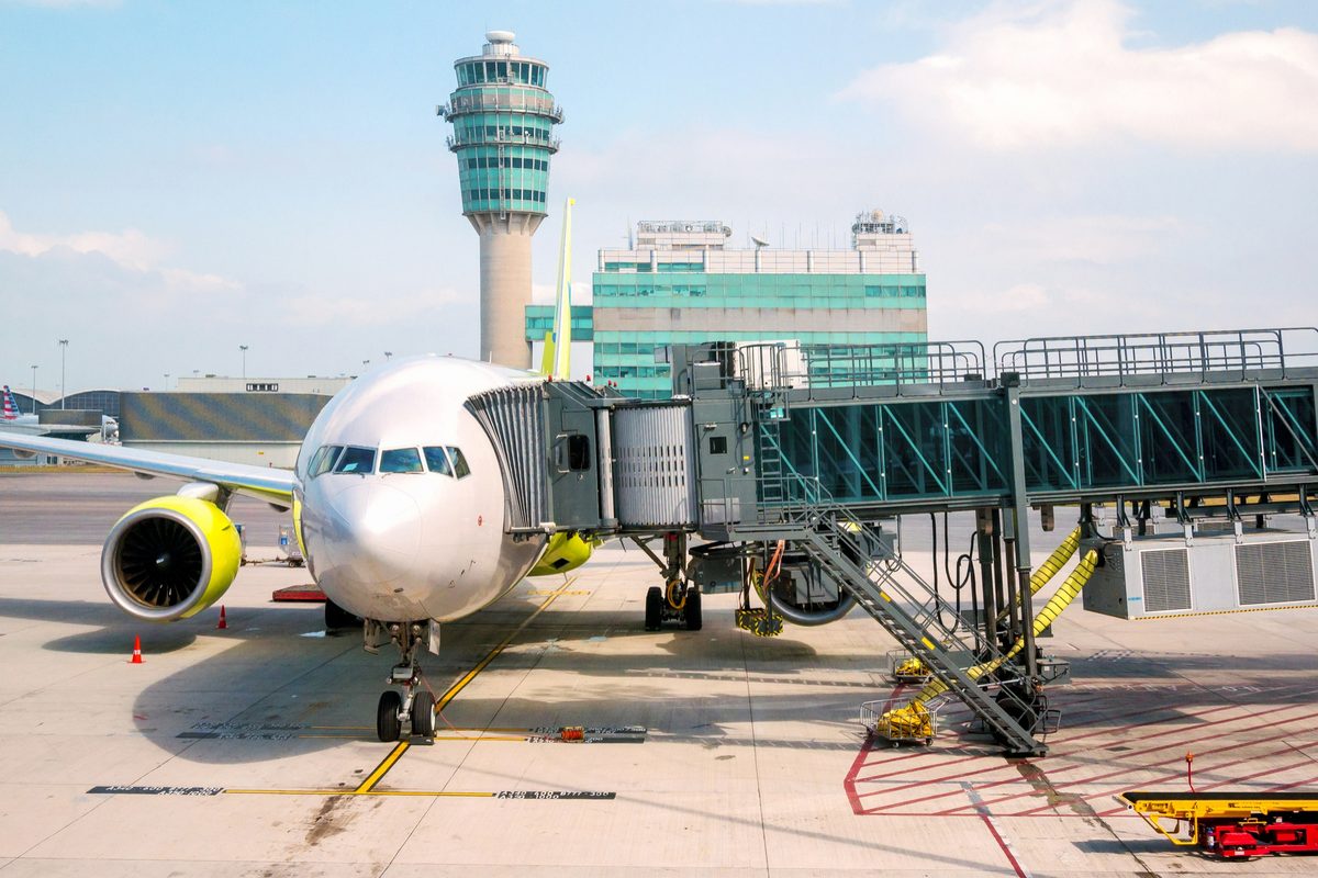 An airliner at the gate beside a boarding bridge, with the control tower behind